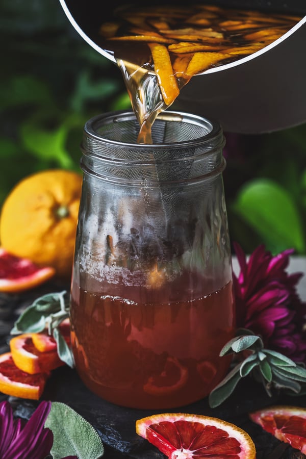 Citrus sage simple syrup being poured through a strainer into a jar