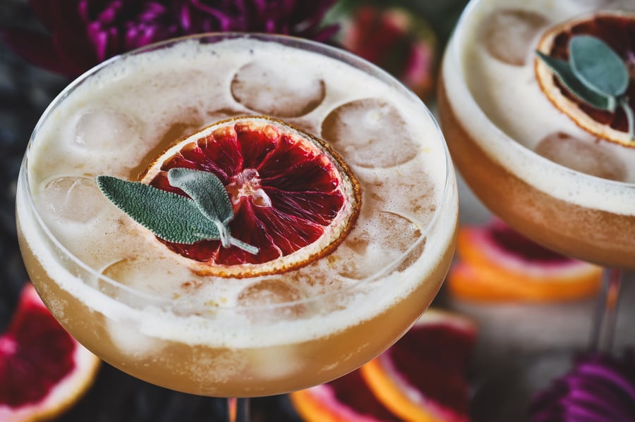 A citrus sage mocktail in a stemmed glass, garnished with dried blood orange and fresh sage leaves