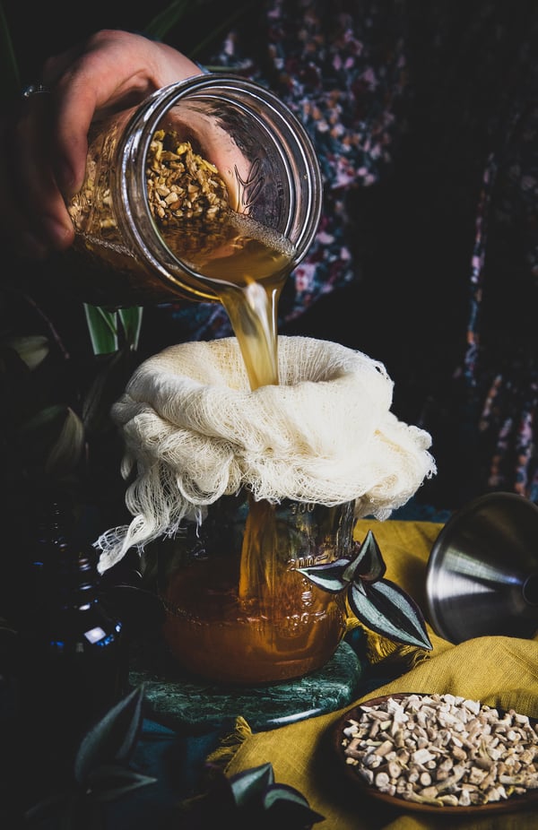 An ashwagandha tincture is strained through cheese cloth into a jar