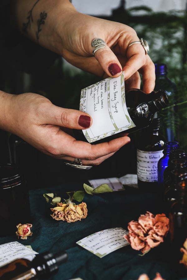 Two hands apply a handwritten label to a bottle of an herbal formula