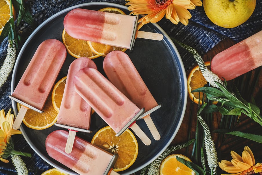 Homemade Creamsicles on a plate surrounded by fresh orange slices and flowers.