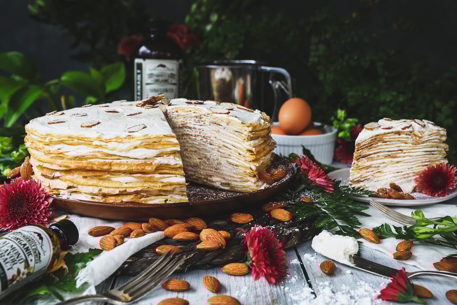 Horizontal photo of almond cream crepe cake with whole almonds and other ingredients around it