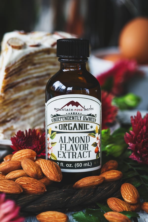 A close up photo of organic almond flavor extract with crepe cake in background