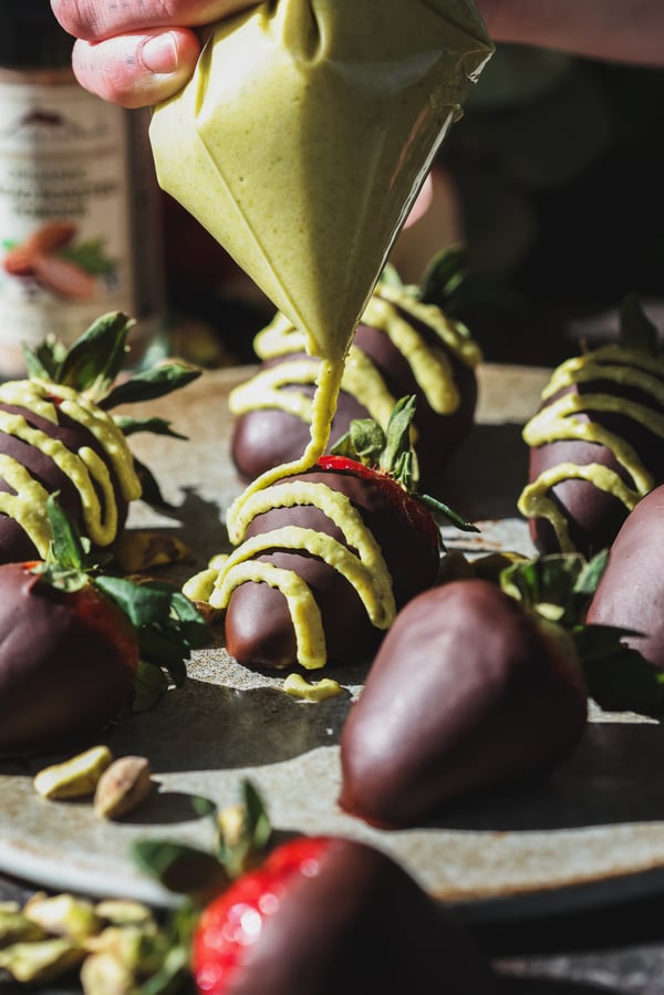 A close up photo of pistachio cream getting drizzled onto chocolate covered strawberries