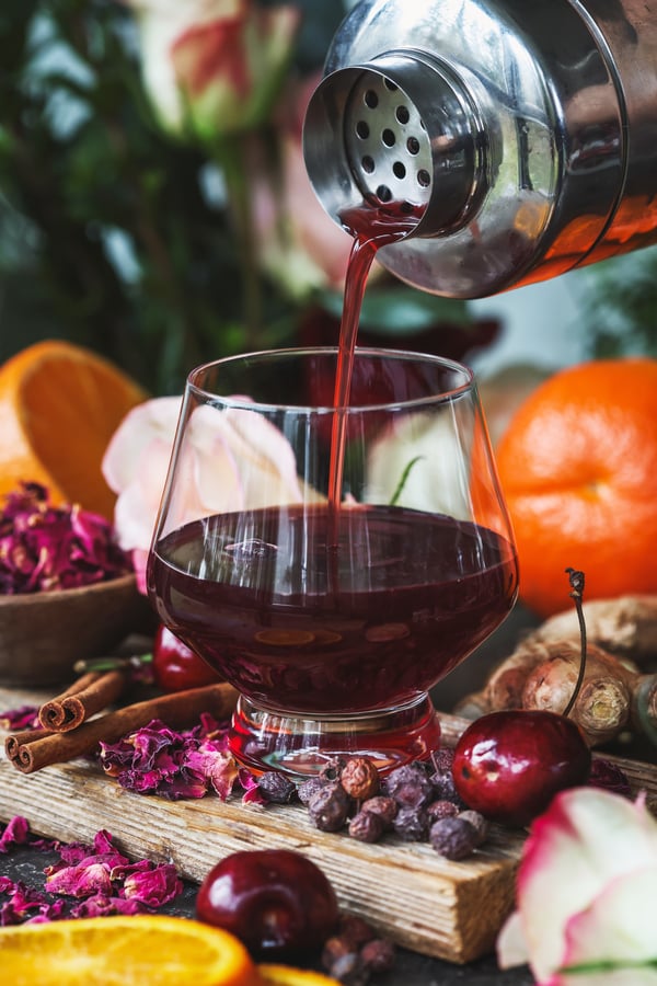 Shaken mocktail being poured from shaker into glass with ingredients around it