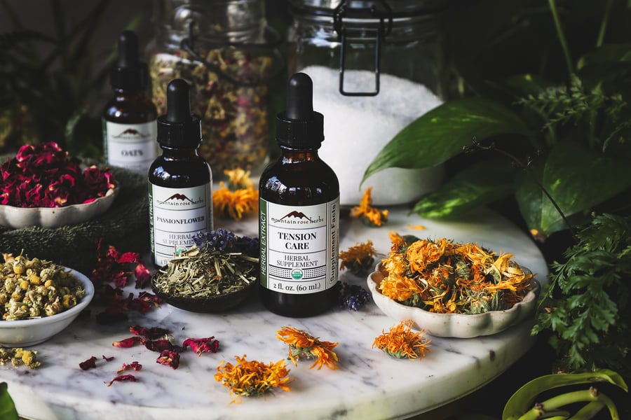 Bottles of calming herbal extracts sit beside herbal bath ingredients on marble surface