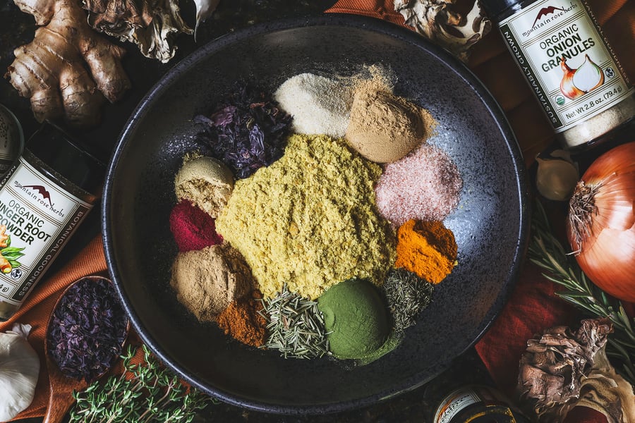 An over head photo of all the ingredients for fire cider bouillon in a bowl with herbs and dried mushrooms around it
