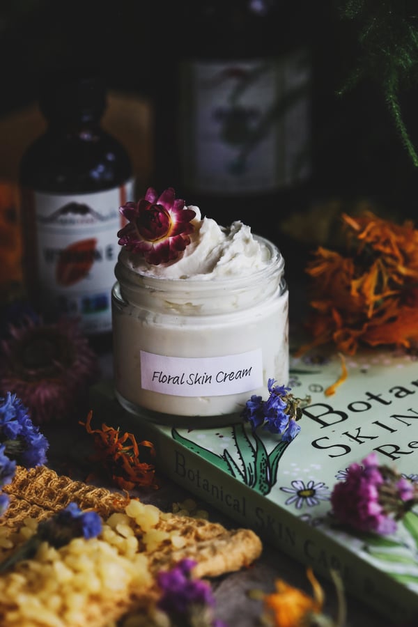 Floral Skin Cream in a clear glass jar-  Surrounded by ingredients used to make it, 