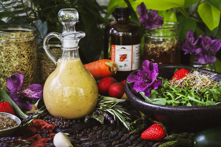 A pour bottle of four thieves vinaigrette sit beside a bowl of greens and other salad fixings