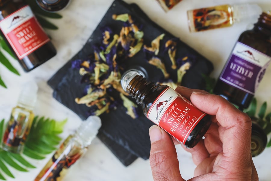 A hand drips sweet marjoram essential oil into a roll top bottle