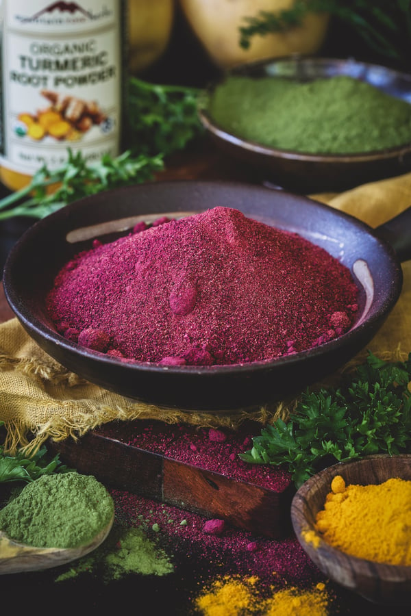 A bowl of beet root powder and assorted other herbal powders with potatoes in the background