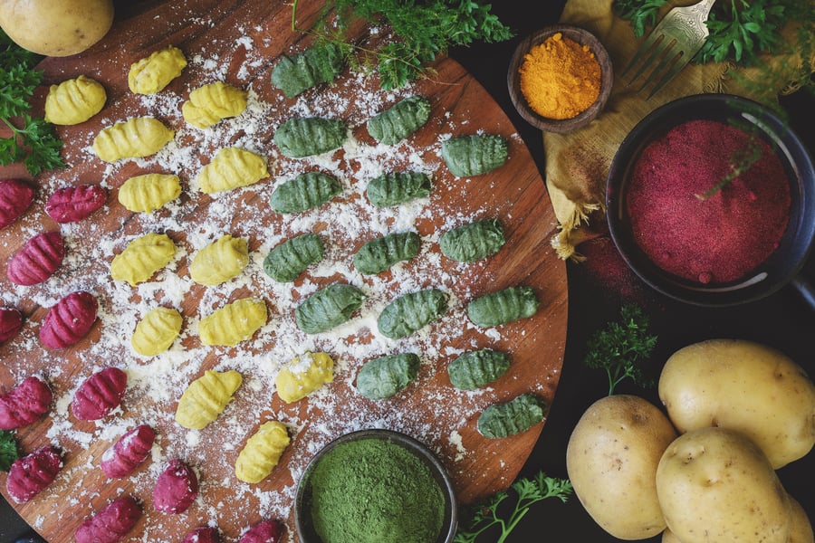 Colorful, freshly rolled gnocchis sit on a floured cutting board