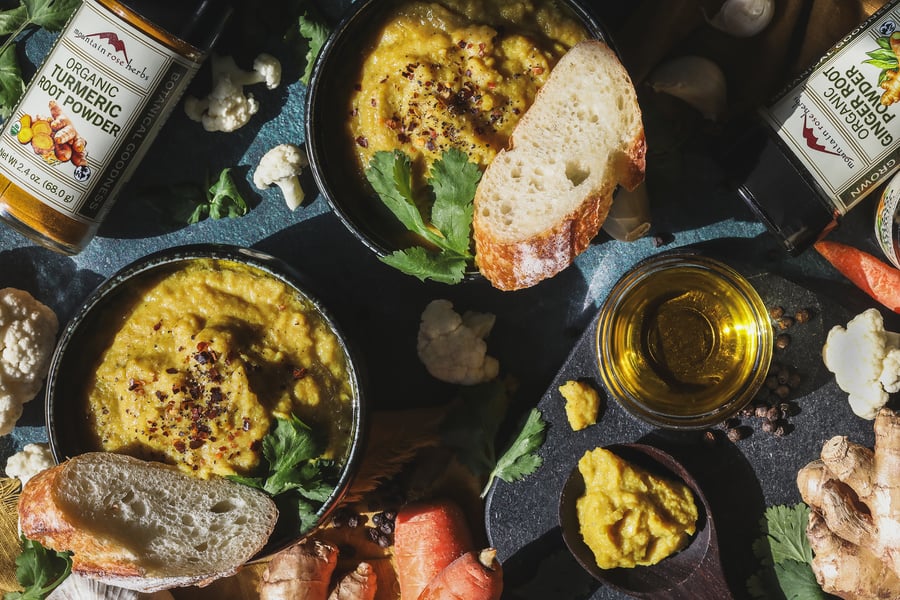 Two bowls of golden soup with bread and ingredients around them