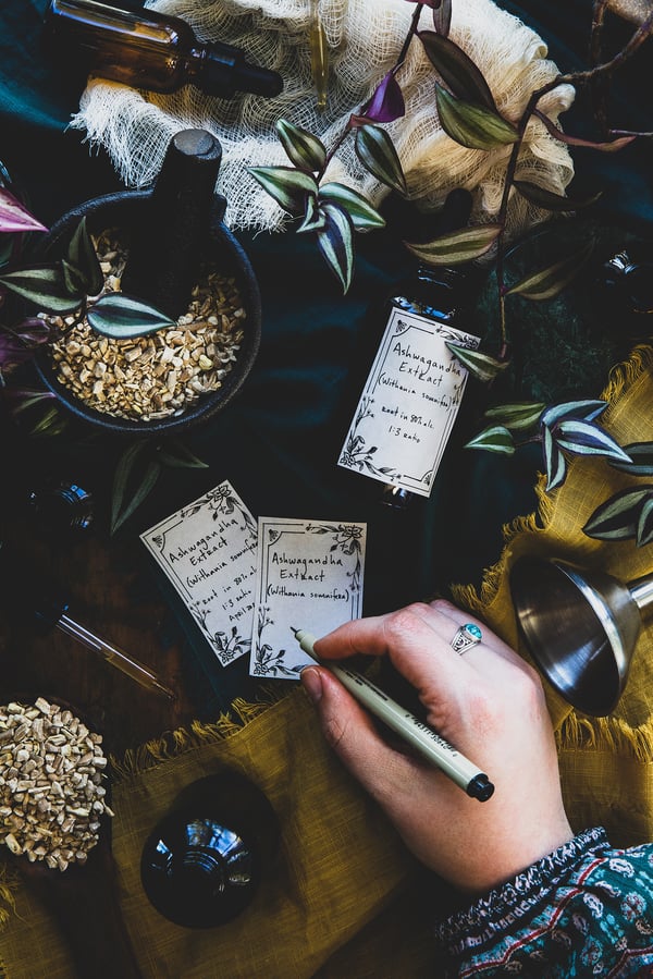 An overhead photo of a hand creating hand written labels for herbal products