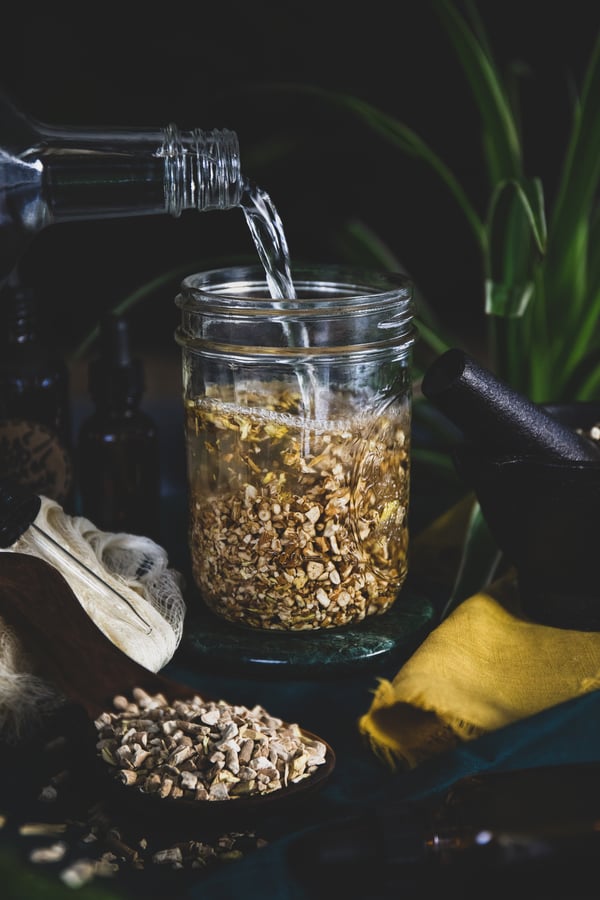 Grain alcohol being poured into a jar with herbs in it to create an herbal extract