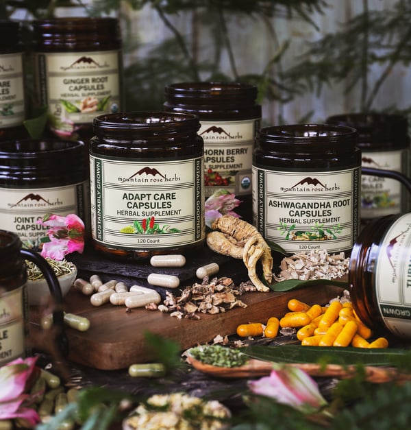 A selection of Mountain Rose Herbs' capsule line sits surrounded by herbs and capsules