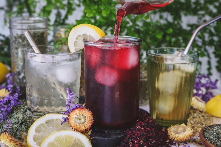 Three iced herbal electrolyte drinks with dried herbs and lemon around them