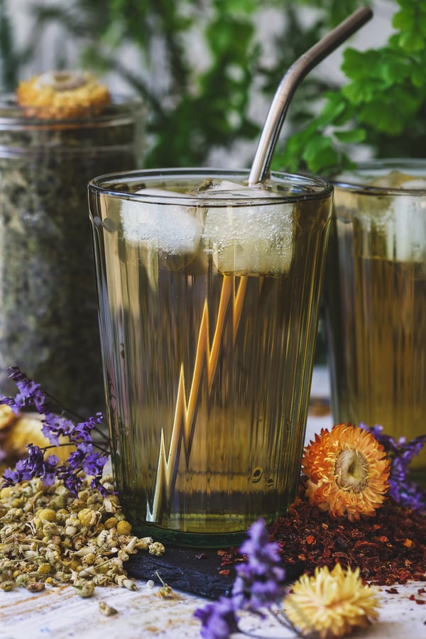 An glass of calming herbal electrolyte chills in a glass with ice and dried herbs around it 