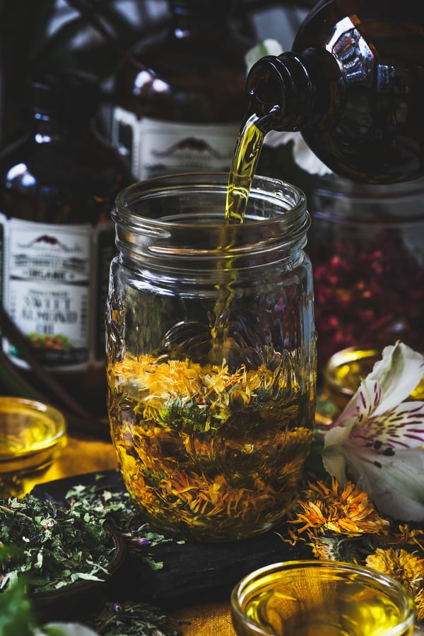 Olive oil being poured into a jar of dried calendula flowers