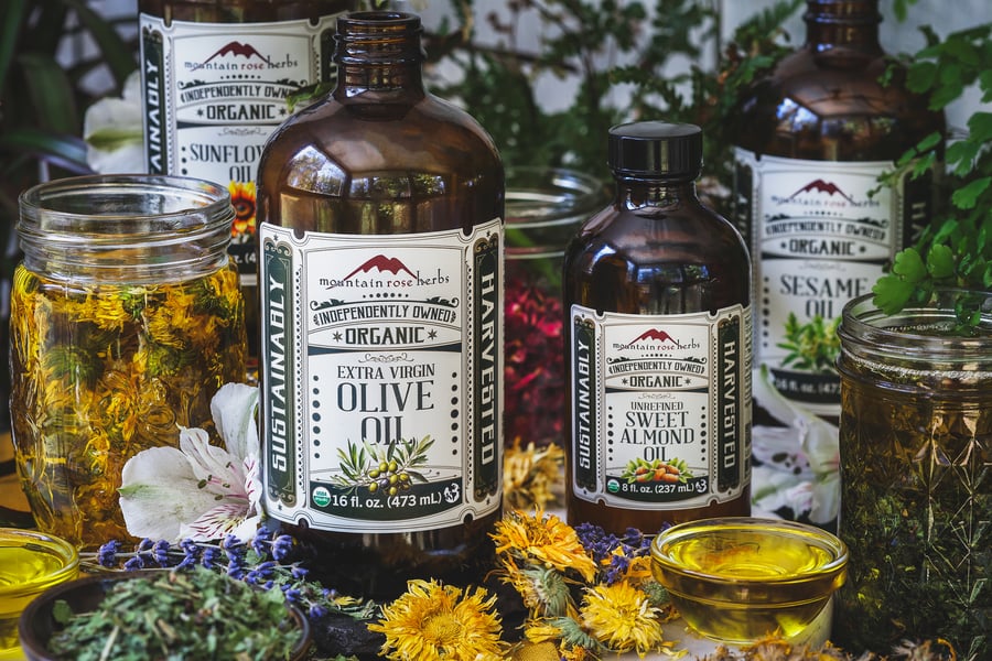 A photo of various carrier oils and dried herbs
