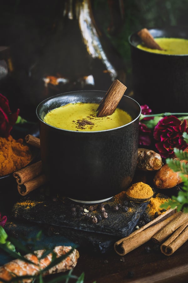 A cup of warm golden milk surrounded with herbs