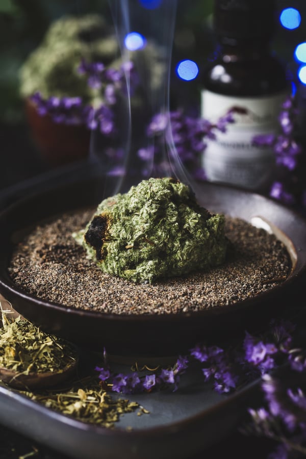 A small pile of dried mugwort in a dish of sand smokes as it is burned