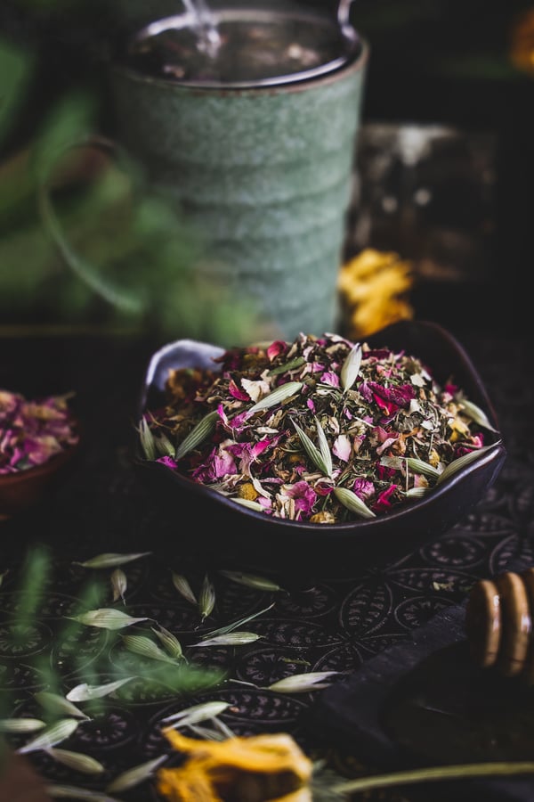 Bowl of colorful herbs include rose petals, oat tops, chamomile flowers