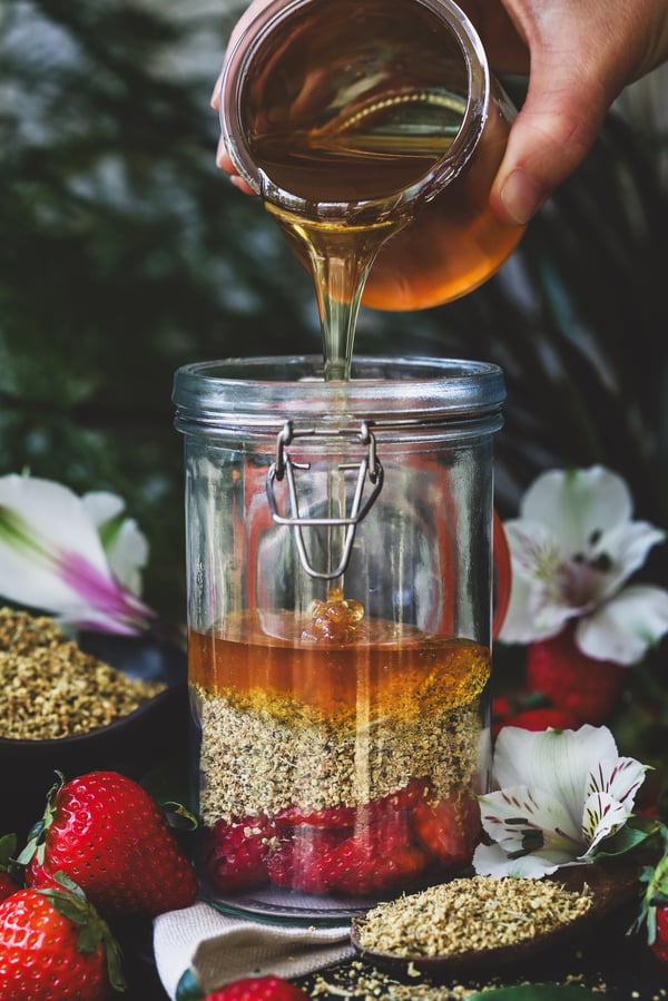 Honey is poured into jar with elderflowers and cut strawberries