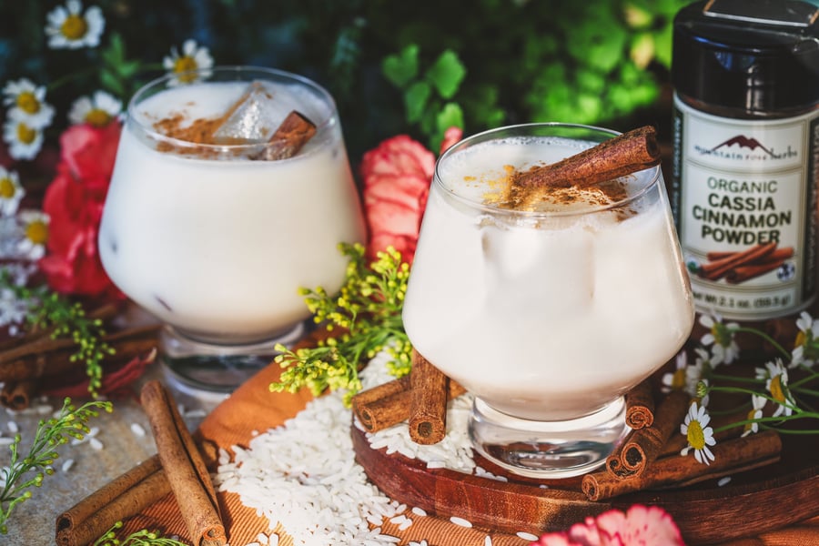 Two iced glasses of horchata sit side by side with rice and cinnamon sticks around it