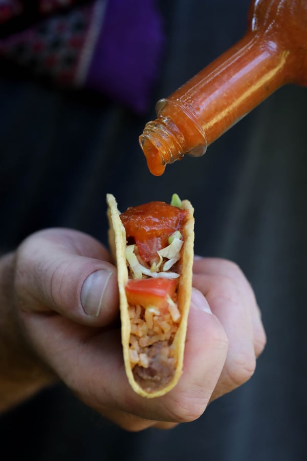 Hand holding a taco while hot sauce is being poured onto it. 