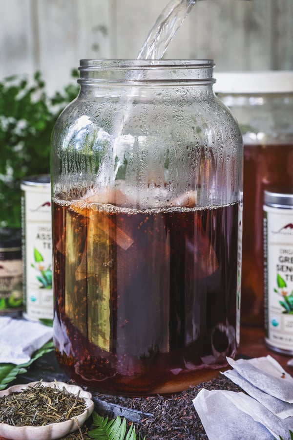 Hot water is poured into gallon jar with tea bags and sugar in it