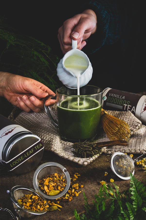 Hand pouring milk into cup of rick green matcha tea. 