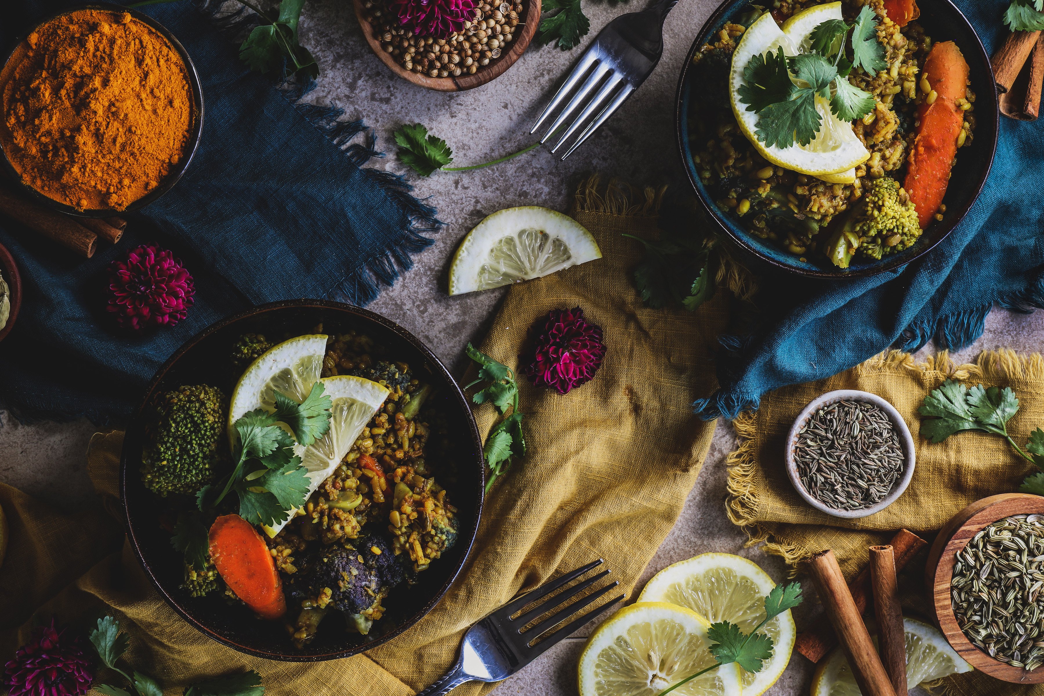 Two bowls of kitchari surrounded by vibrants spices and fresh lemon slices. 