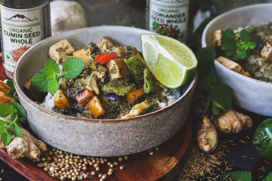 Two bowls of hot lemon balm curry with ingredients around them
