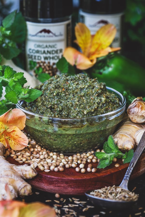 A bowl of lemon balm curry paste with ginger root and coriander seeds around it