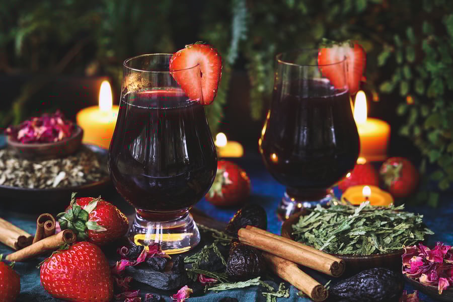 Two glasses of lucid dreaming cordial sit in candlelight with ingredients around them