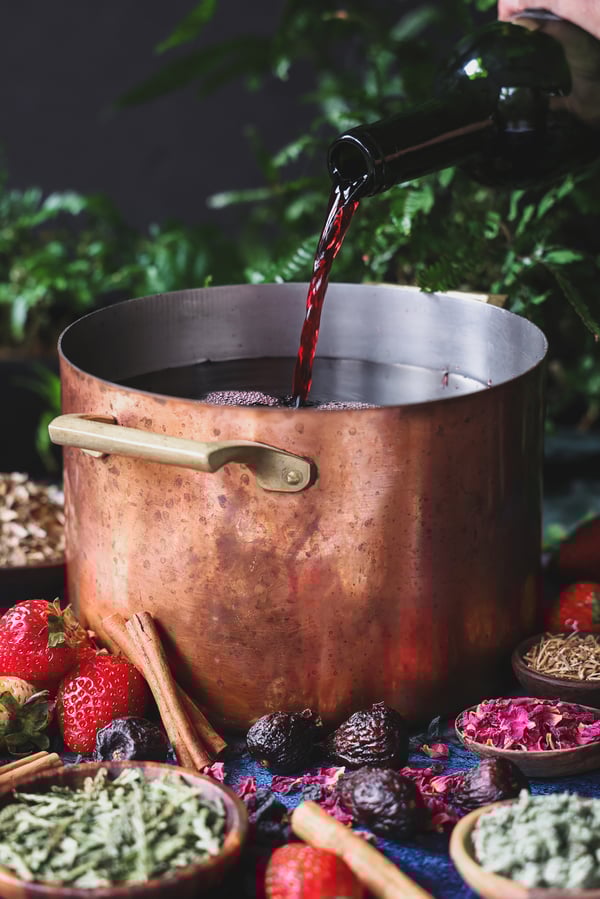 Red wine is poured into a copper pot, ready to heat with herbs and fruit