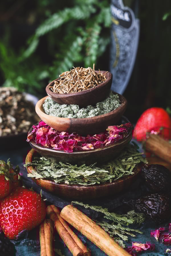 A stack of dried herbs in bowls with fresh strawberries and dried figs around it