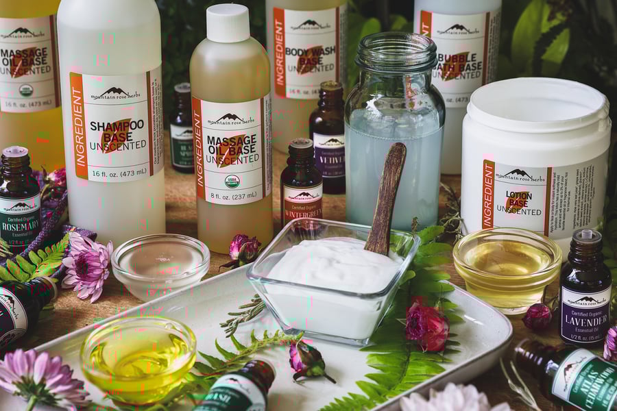 The Mountain Rose Herbs unscented base line products on a table with essential oils and flowers around them