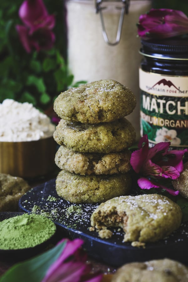 A stack of matcha sugar cookies with flowers and matcha around it