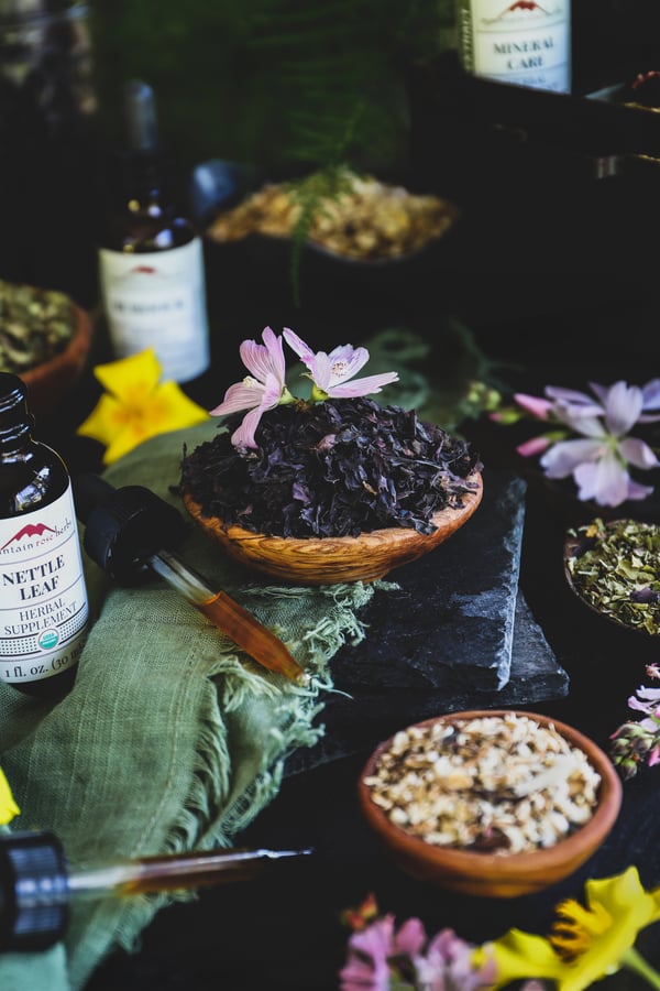 A selection of extract and dried herb sit out on a counter surrounded with flowers