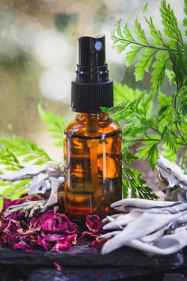 A toner blend in a mister bottle surrounded by red rose petals and white sage. 