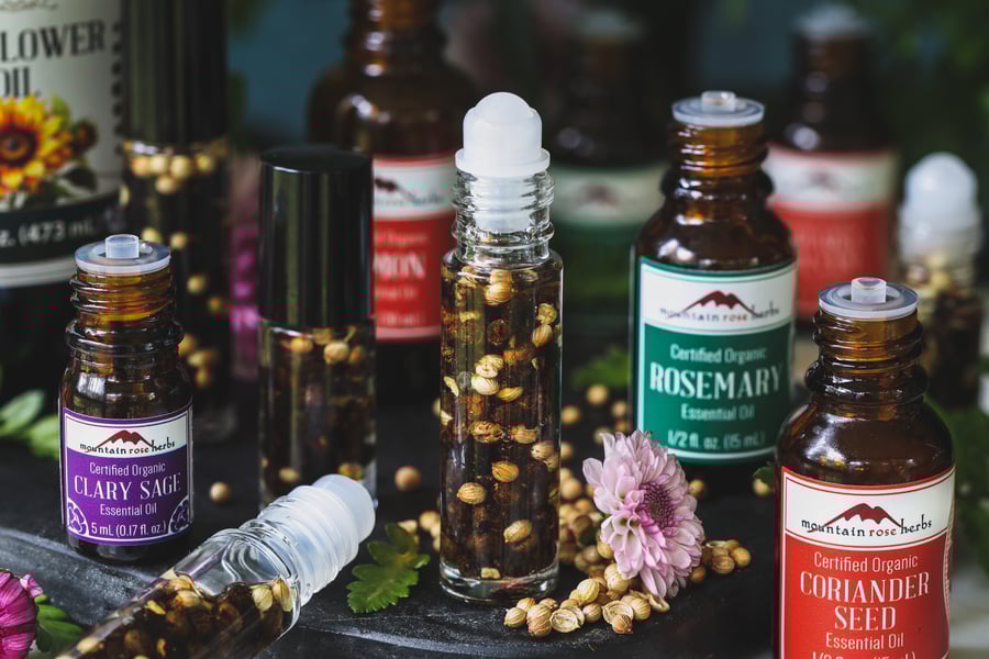 A roll on bottle of of new moon perfume with essential oils and coriander seeds around it