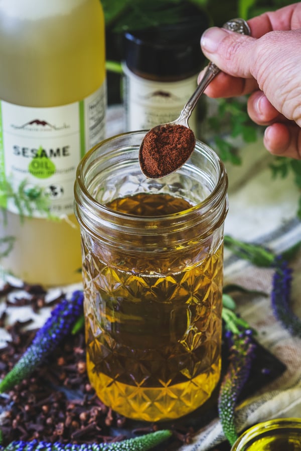 Clove powder being sprinkled into a jar of sesame oil