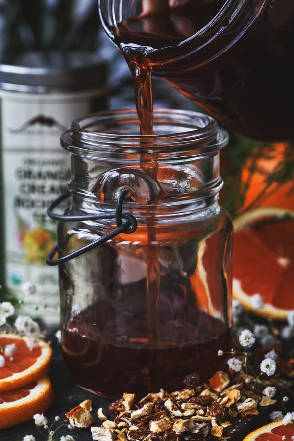 Orange cream rooibos simple syrup being poured into a glass clear jar for storage