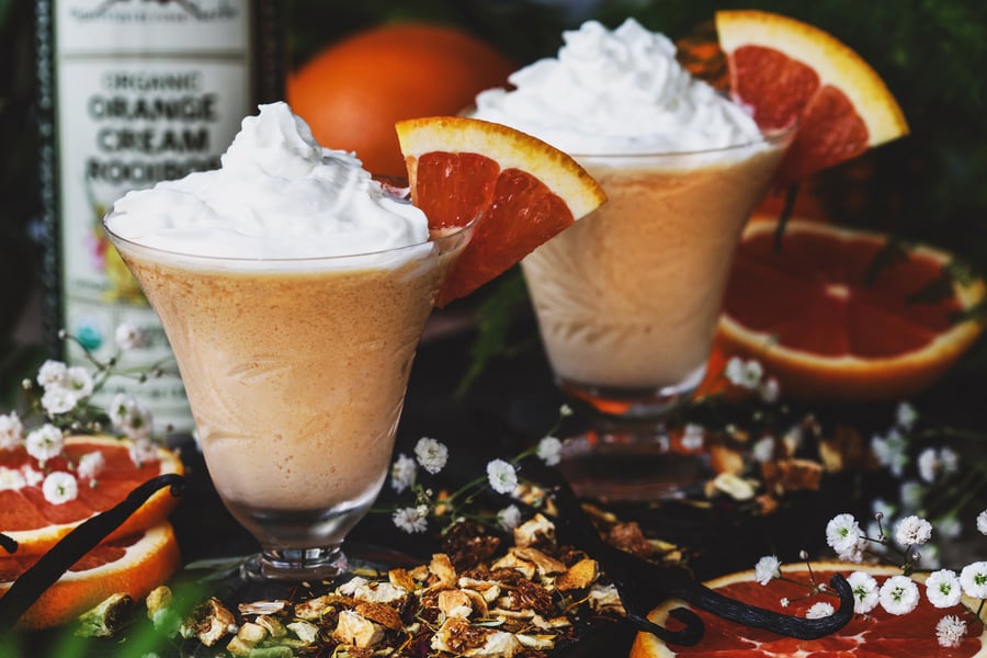 Two orange cream rooibos slushy mocktails in glass cups topped with whipped cream and garnished with orange slices