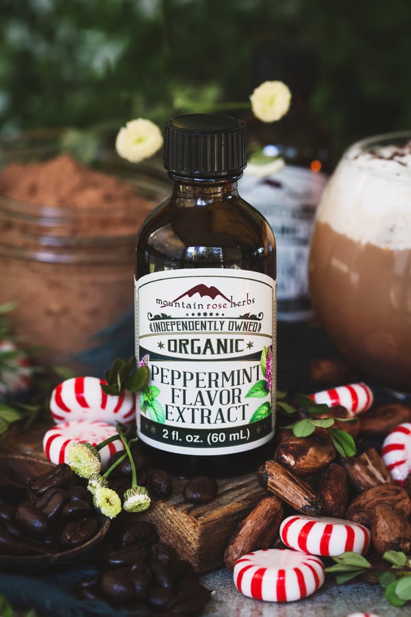 A bottle of peppermint flavor extract with cacao and coffee beans around it