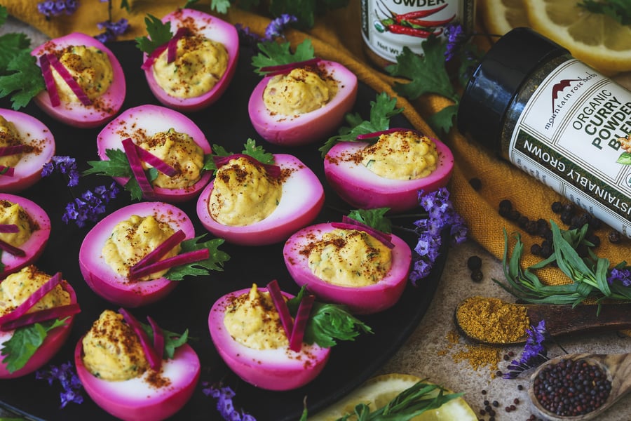 A plate of deviled eggs with garnishes with spices nearby