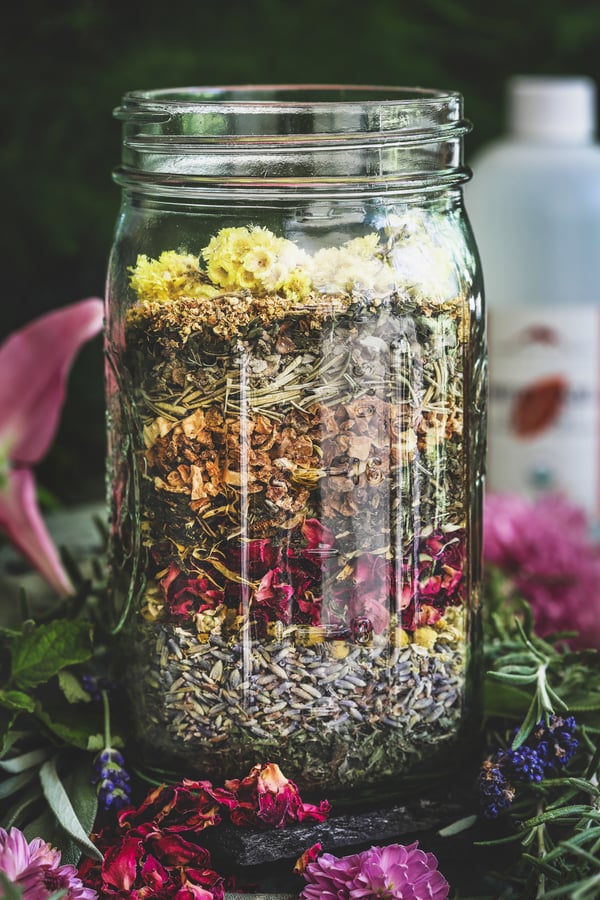 Colorful herbs stack up inside a jar awaiting the addition of witch hazel