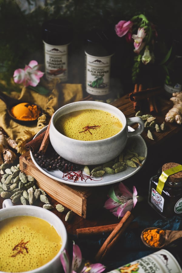 A cup of hot, freshly made saffron golden milk sits surrounded by spices 